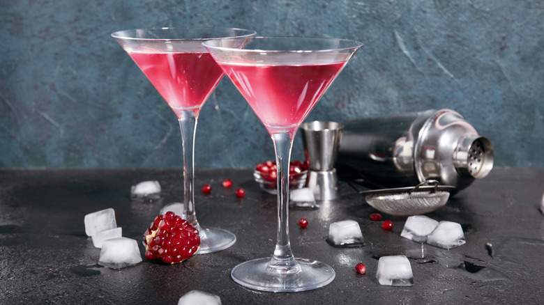 Two pomegranate cosmopolitans in glasses, surrounded by ice cubes and pomegranate seeds