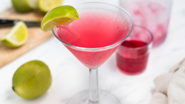 A bright pink cosmopolitan in a glass with a lime wedge