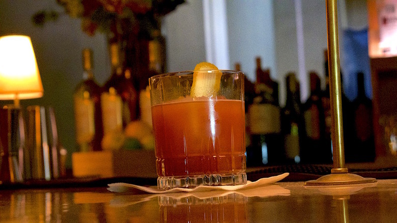 A red Jack O'Groni cocktail in a glass on a bar, with an orange peel garnish