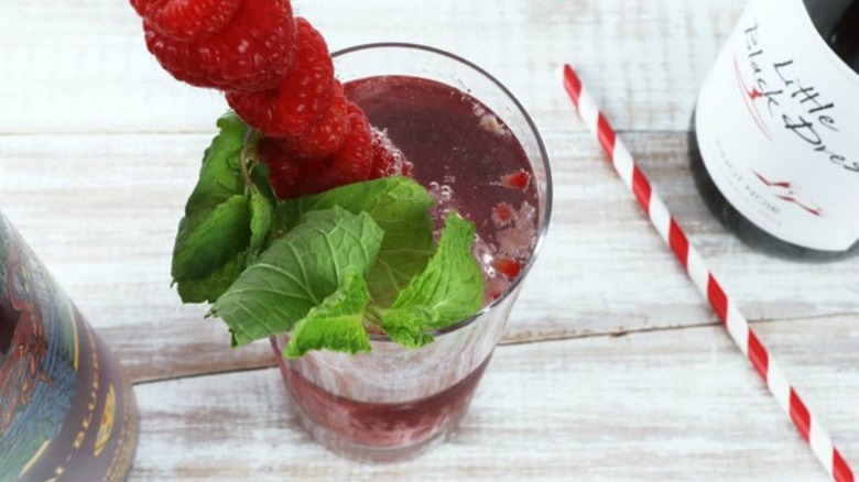 Dark red winter's thaw cooler punch in a glass, garnished with raspberries and mint leaves