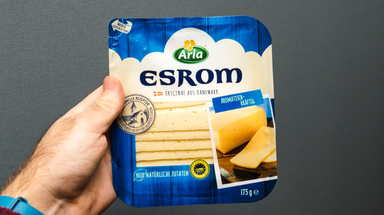 Hand holding a container of esrom cheese