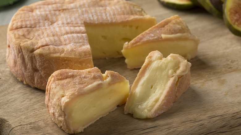 Cut wheel and wedges of munster cheese on cutting board
