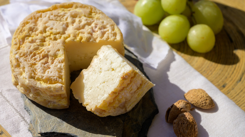 Sliced wheel and wedge of serpa cheese on a stone board, with grapes