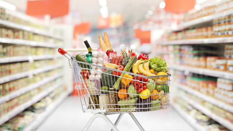 A full grocery cart in grocery store aisle.