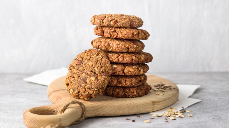 A stack of vegan oatmeal cookies on a beige wooden cutting board, against a white background