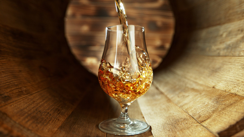 Rum pouring into a stemmed glass that's sitting in a barrel