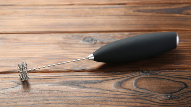 Handheld milk frother sitting on a rustic wood tabletop