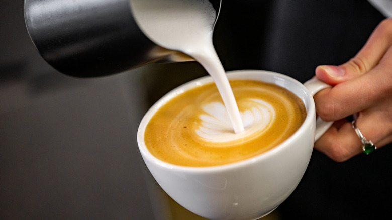 hand pouring foamy milk from a pitcher into a cup of espresso