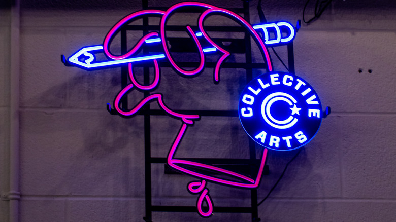 A neon sign for Collective Arts Brewery, featuring the logo on a pink hand gripping a purple pencil