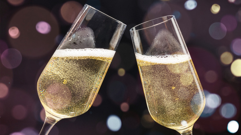 A close-up of two Champagne flutes about to clink together, each about 2/3 filled with bubbling yellow champagne