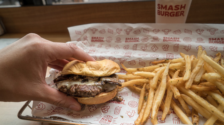 Hand holding a smashburger on a tray with fries