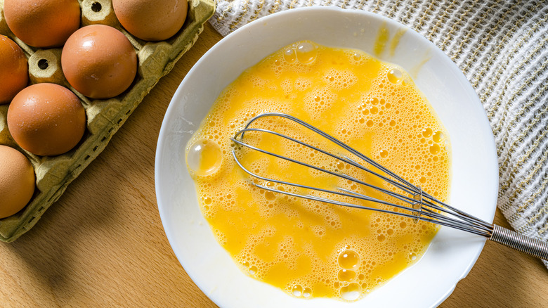 A large bowl of raw scrambled eggs with unbroken eggs to the side