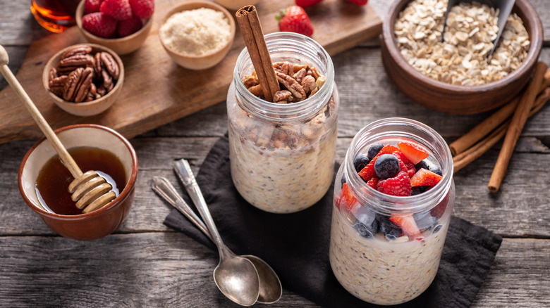 Open jars of overnight oats with assorted berries, nuts, cinnamon sticks, and honey