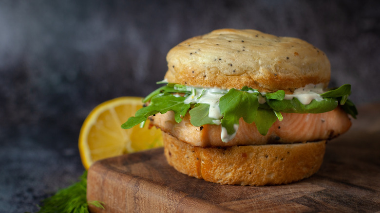 Salmon filet burger topped with arugula and dill aioli on bun.
