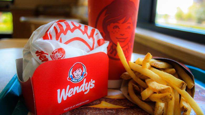 A Wendy's meal on a dine-in tray, with a neatly-wrapped burger, a drink in a red cup with the Wendy's logo on it, and a small order of French fries