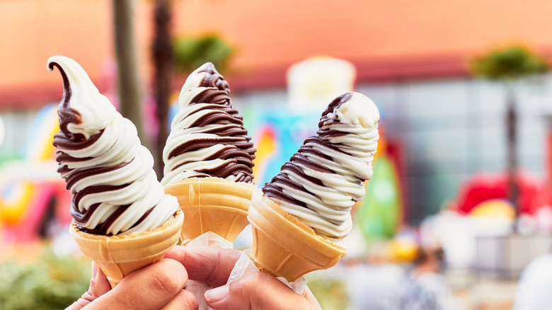 Hands holding soft serve vanilla and chocolate ice creams in sugar cones