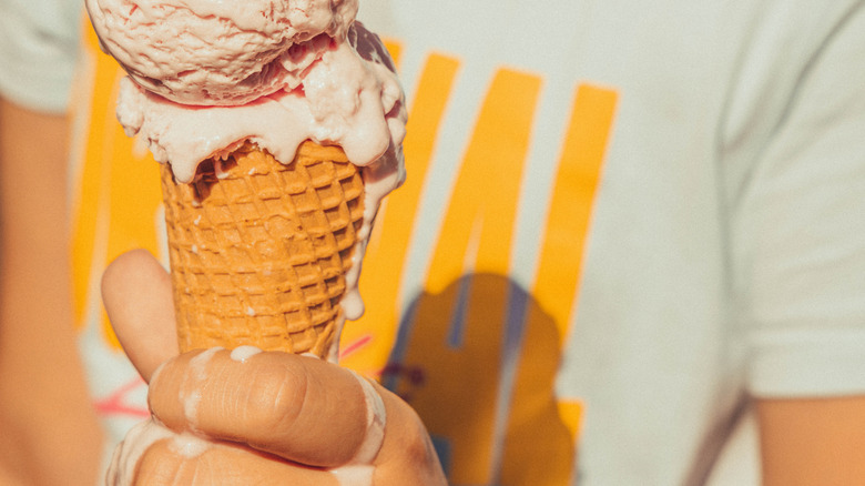 an pink ice cream cone drips down the hand and cone of a child