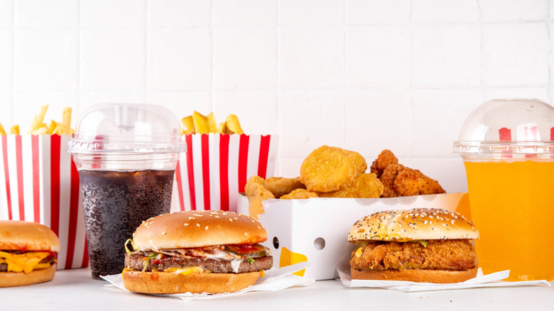 A fast food burger, chicken sandwich, chicken nuggets, french fries, and two drinks on a table