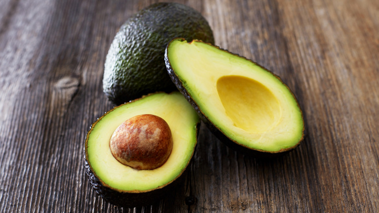 Avocados whole and halves on a wooden table.