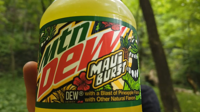 A closeup of a bottle of Mountain Dew Maui Burst, featuring pineapples, flowers and a description noting pineapple and other natural flavors