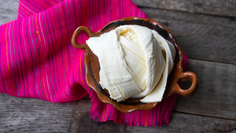 overhead shot of Mexican Oaxaca cheese in a clay dish on a colorful napkin