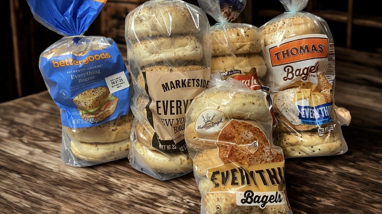 Five bags of store-bought bagel brands on a wooden table.