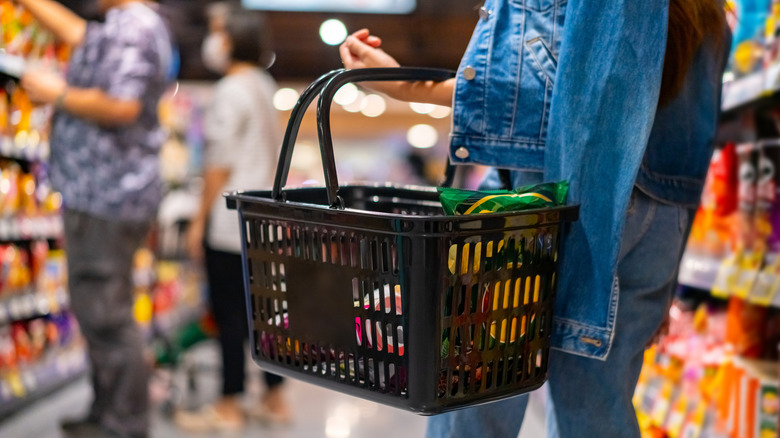 Shopper holding a hand basket of groceries in supermarket