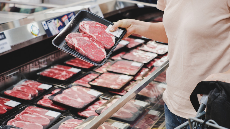 Shopper picking up package of raw steaks in meat department