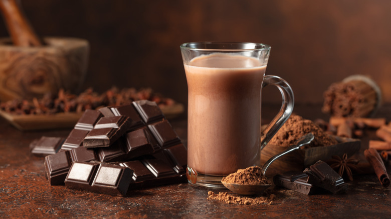 Chunks of chocolate on a brown tray next to a glass cup of hot chocolate