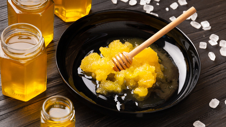 Crystallized honey in a black plate alongside jars of honey on a table.