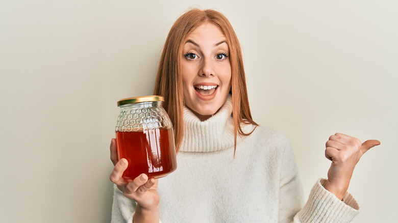 A woman holding a jar with honey pointing thumb up.