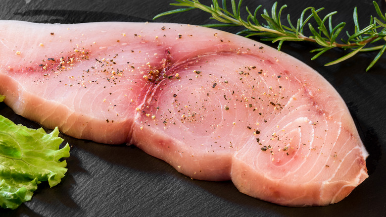 Close up of raw swordfish steak with pepper and herbs on a slate table.