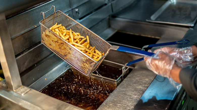 Person holding fryer basket full of fries over deep fryer