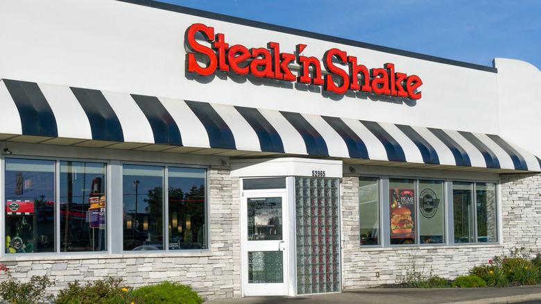 The exterior view of a Steak 'n Shake with red logo and black and white striped awning.