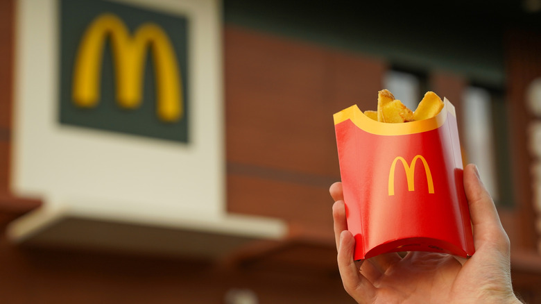 Hand holding french fries in front of McDonald's restaurant