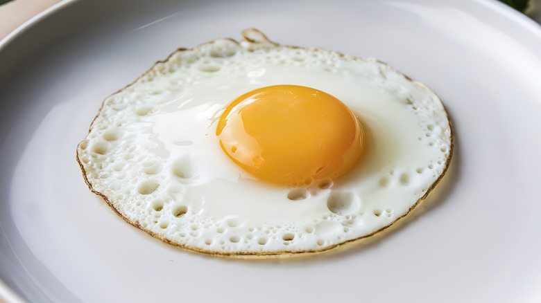 A sunny-side-up egg with vibrant yellow yolk and crispy edges on a white plate.