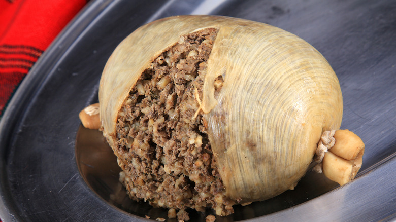 A large haggis with a slit in cut into the casing, allowing the crumbled meat and oatmeal filling to spill out.