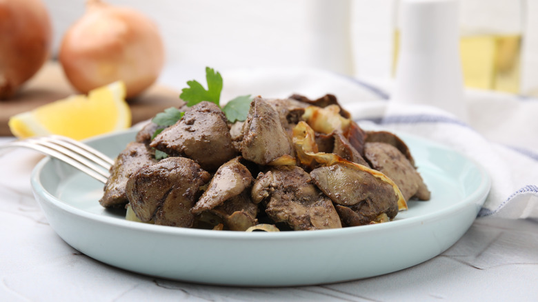 A plate of liver and onions on a table with onions and lemons in the background..