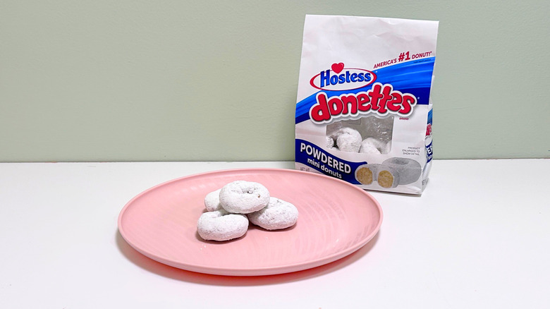 A bag of Hostess Powdered Donettes next to a pink plate with donuts