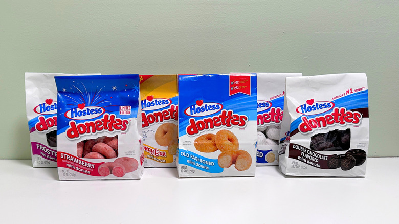 Six bags of Hostess Donettes lined up against a green and white background