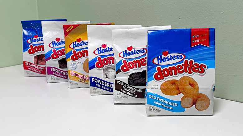 Six bags of Hostess Donettes lined up against a green and white background