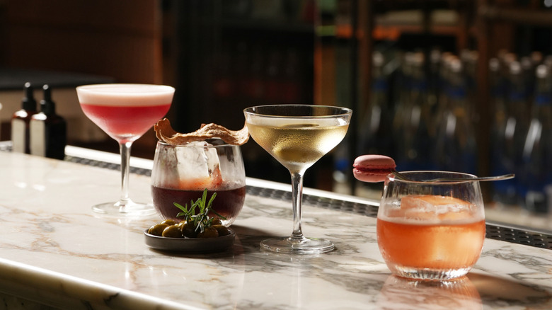 Assorted cocktails of various colors lined up on a marble bar
