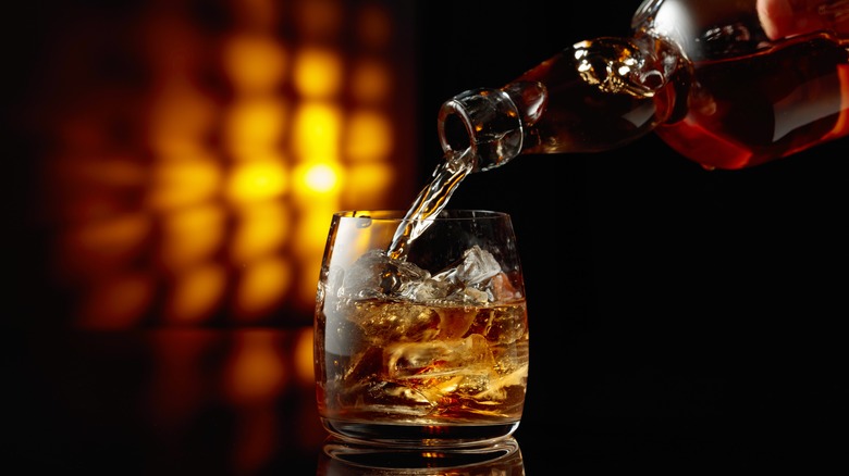 pouring bourbon into a glass with ice