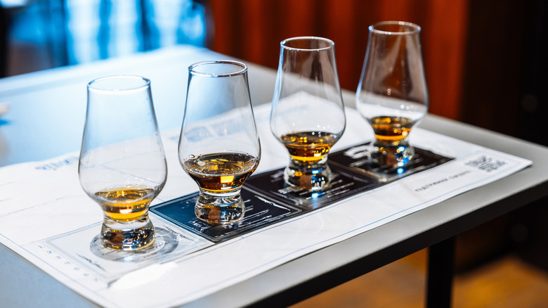 A flight of four tasting glasses with whiskey