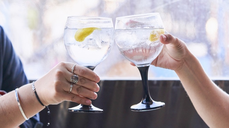 A closeup of two hands cheersing vodka cocktails together in front of a window