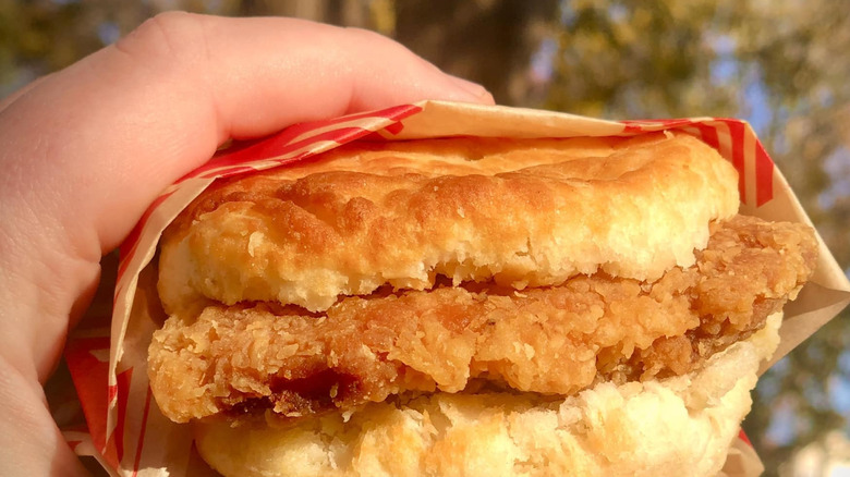 a chicken biscuit wrapped in Bojanles wax paper held up against the sky.