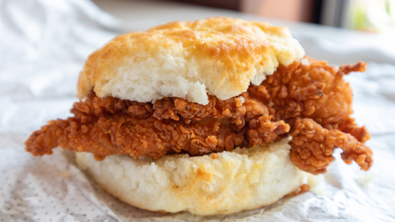 A cast iron skillet packed with a batch of fresh made biscuits sitting next to a board with rounds of biscuit dough being cut out.