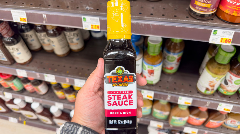 Texas Roadhouse steak sauce being held in front of a grocery store shelf