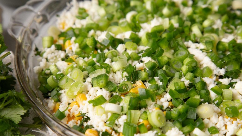 crumbly white cheese with green onions and corn in a clear pie plate