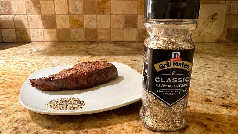 container of seasoning next to plate with steak